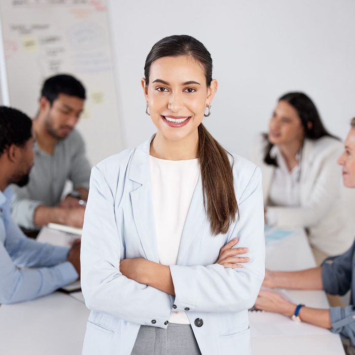 Cropped portrait of an attractive young businesswoman standing with her arms folded in the boardroom and her colleagues in the background.